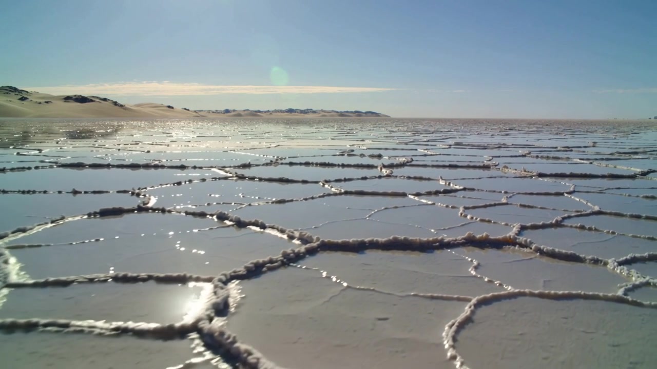 Et bevegelig kamera avslører polygonal salt skorpe og grunne, skinnende bassenger på en saltslette, fremhever rygger.