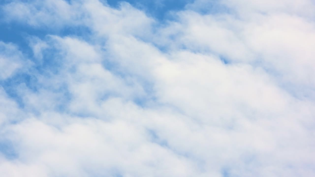 Timelapse of white clouds drifting quickly across bright blue sky on sunny day.