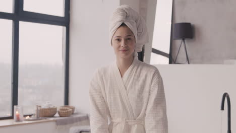 front view of a woman sitting posing and smiling at the camera with a towel on her head and a bathrobe