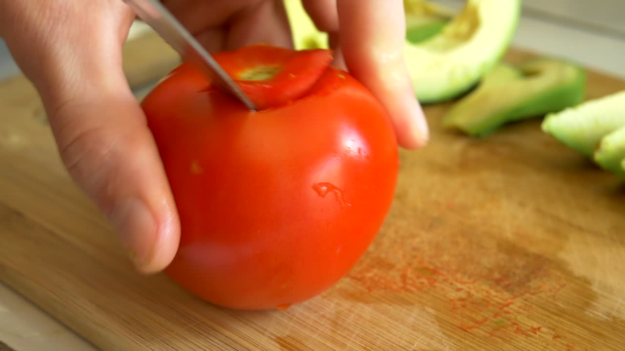 요리사는 부엌에서 건강한 채식주의 점심을 만드는 동안 나무 대나무 커팅 보드에 잘 익은 빨간 토마토를 준비합니다.