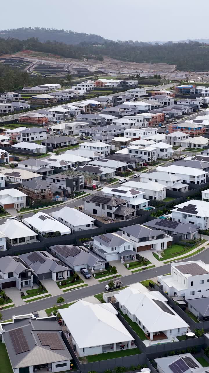 Un dron se desliza sobre casas suburbanas contemporáneas, revelando un telón de fondo montañoso, iluminación nublada y calles organizadas