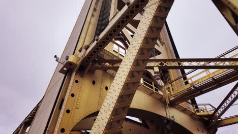 low angle footage of crossing beams on a rusty yellow bridge in downtown sacramento, california with a grey sky in the background