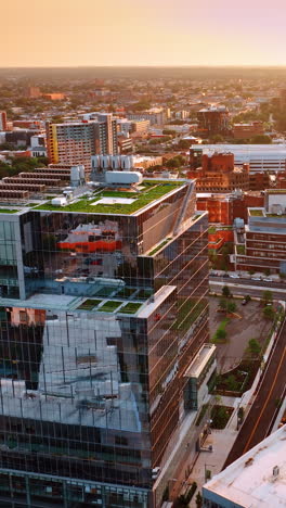 approaching modern glass building with green zone on top. philadelphia cityscape from air at sunset. vertical video