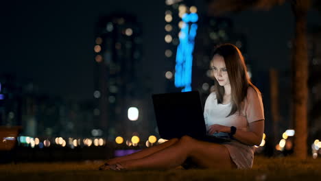 young beautiful girl designer working remotely on a laptop on the street in the summer under palm trees at night in the city park. united arab emirates european woman at night in dubai