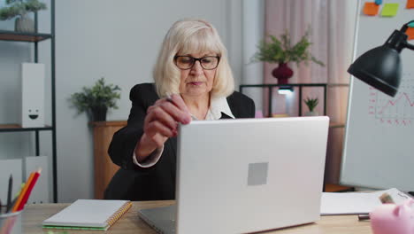 senior mature older business office woman elearning online writing notes from laptop, live webinar