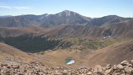 Viewing-lake-and-high-mountain-peak-in-Colorado-across-a-valley,-tilt