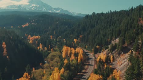 4k aerial country road in colorful forest in fall with snowy mountain in background drone tilt up