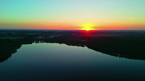 a reveal shot of a colourful sunset view at a lake by a forest landscape