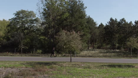 Person-walking-along-country-road-with-motorcyclist-driving-past,-aerial-view-open-to-view-over-a-big-mining-area