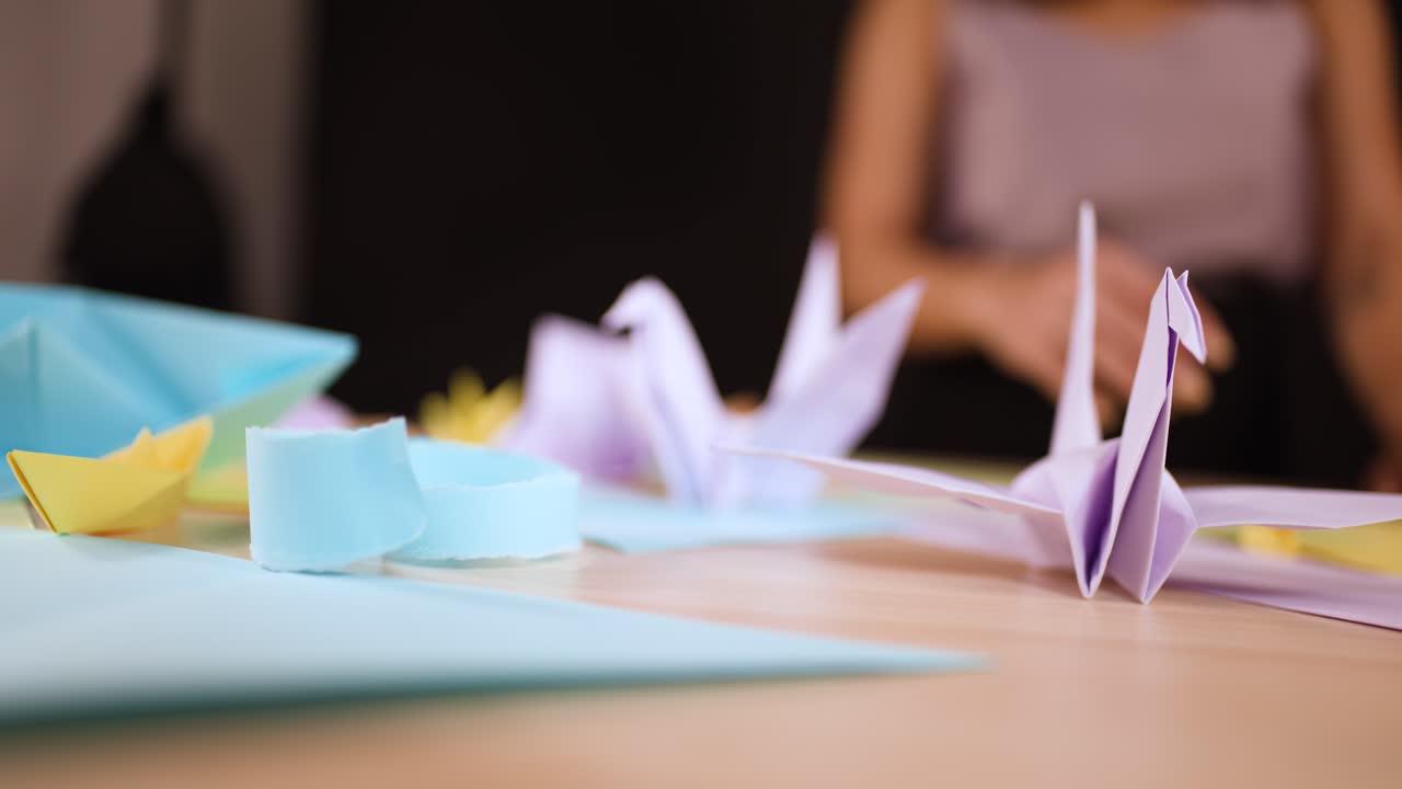 Primo piano di mani che posizionano gru di carta fatte a mano su un tavolo con illuminazione soffusa