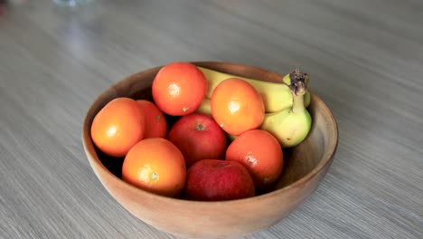 person choosing fresh apple from fruits bowl placed on wooden table, nested sequence