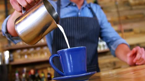 camarero vertiendo leche en el café en el mostrador