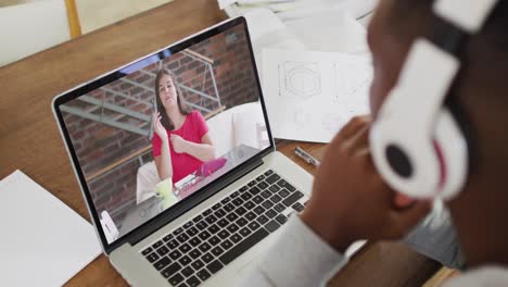 African-american-businessman-sitting-at-desk-using-laptop-having-video-call-with-female-colleague