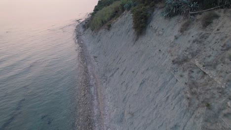 aerial tilt-up shot showing the sea and sandy cliffside with medicinal mud coast of arillas, corfu, greece