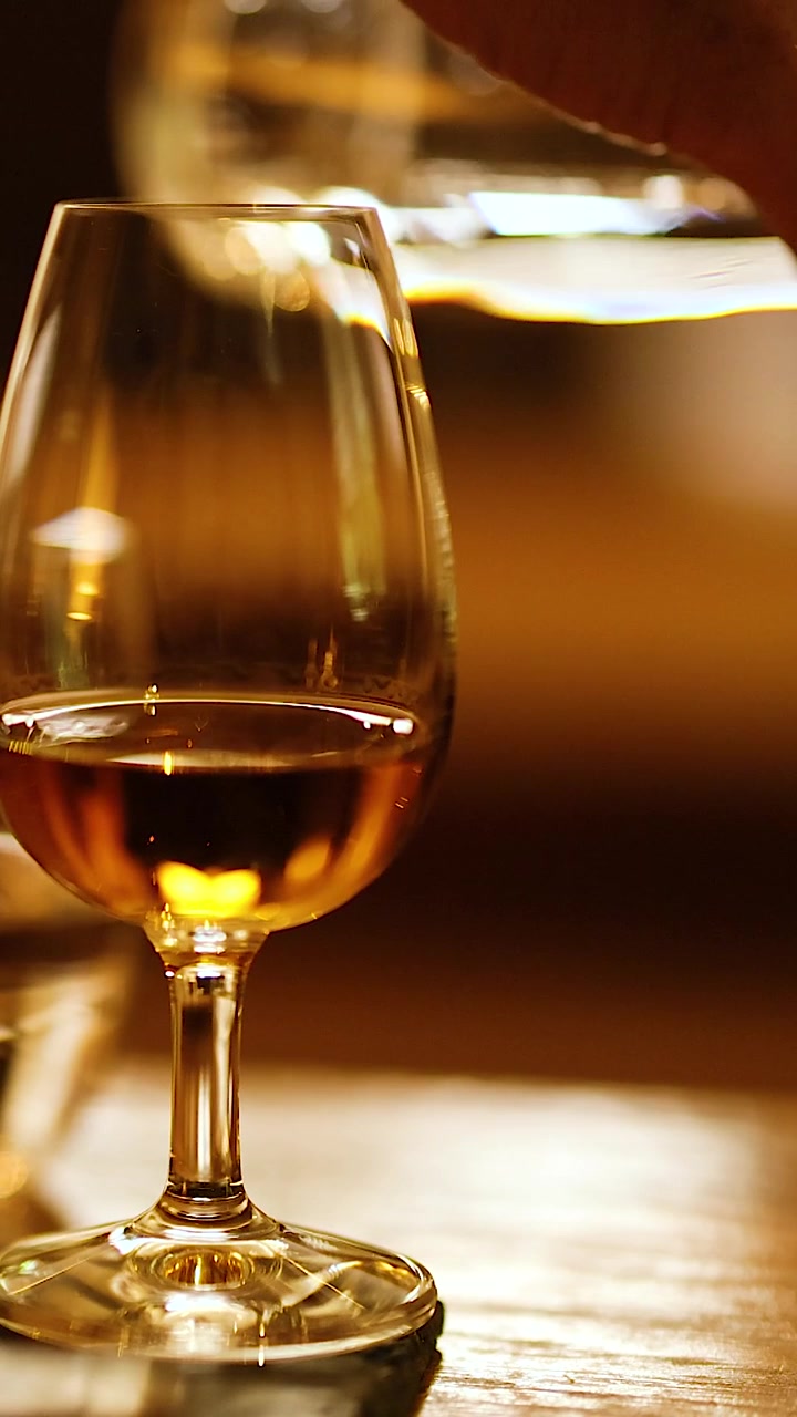 Uno scatto verticale ravvicinato di liquido dorato in un bicchiere durante un evento di degustazione di distillati.