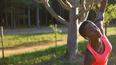 female athlete performing stretching exercise while listening music in forest 4k