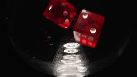 small red dice falling into empty glass at bright light