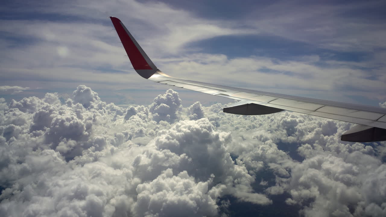 Vue depuis le hublot d'un avion montrant l'aile au-dessus de nuages spectaculaires dans le ciel pendant une scène de voyage en avion avec une lumière du jour éclatante et un paysage nuageux doux.
