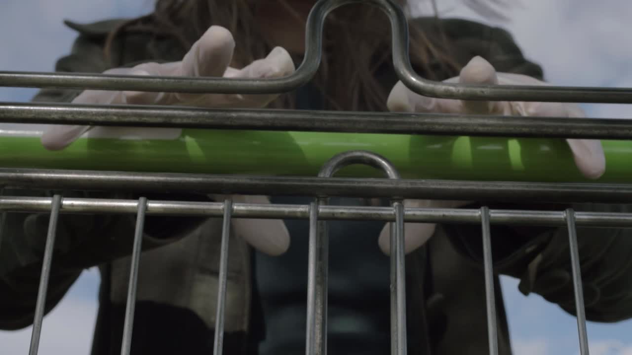 Hands pushing shopping cart handle wearing hygiene gloves