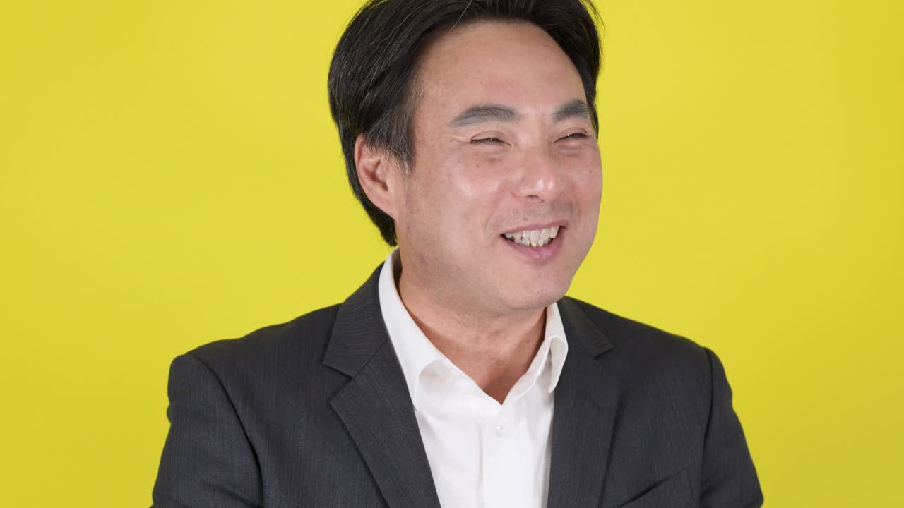 Businessman in suit smiles, talks, and gestures confidently in bright studio lighting, yellow backdrop