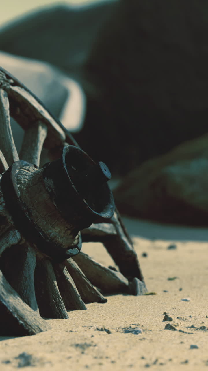 Old wooden wagon wheel resting in sand near rocks by the shore