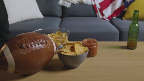 persona en casa viendo un partido de fútbol americano en la televisión con bebidas, bocadillos y pelota 3