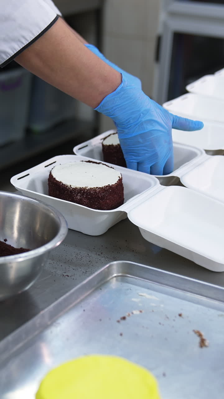 Cake production in the food factory. Confectioner puts the small cakes into individual packaging. Vertical video