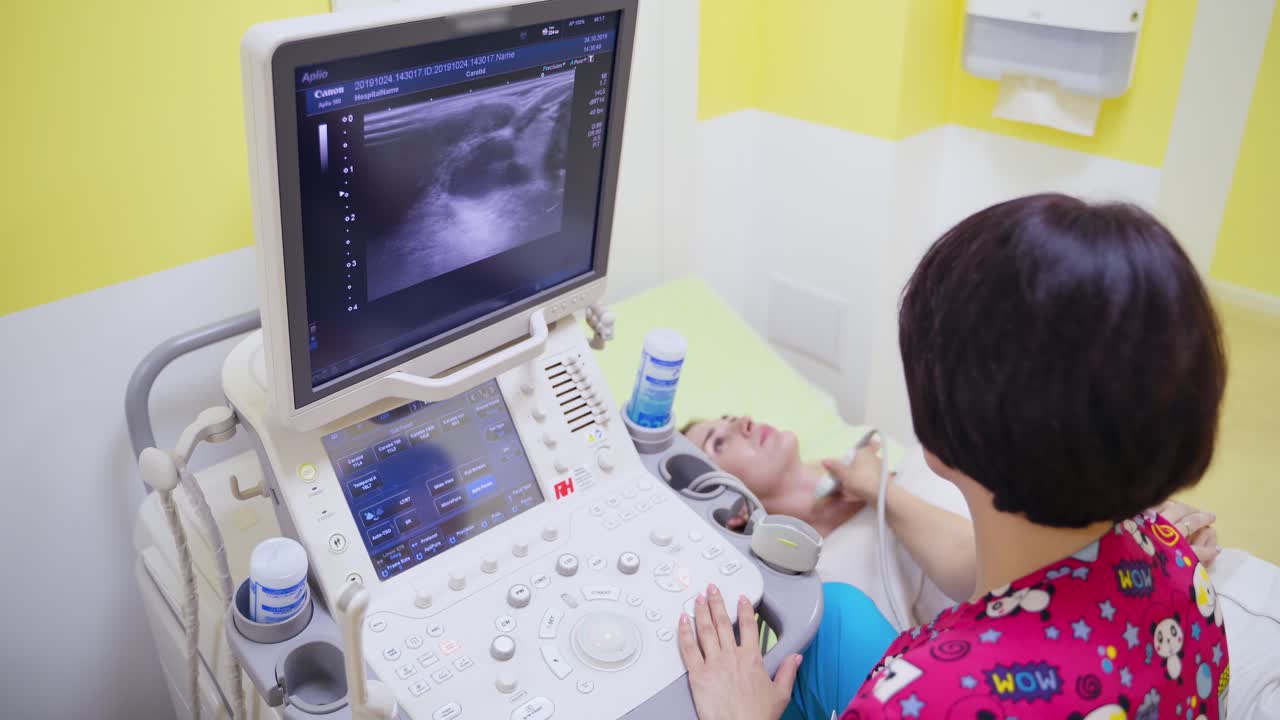 Doctor makes ultrasound diagnostic. Woman specialist using ultrasound scanner in clinic. Doctor runs ultrasound sensor on neck and looking at screen.