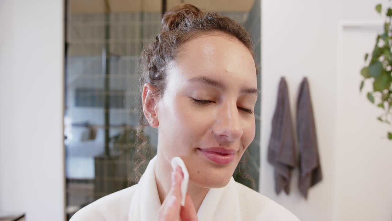 Donna applica tonico viso con un dischetto di cotone, godendosi la routine di cura della pelle a casa.