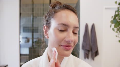 applying facial toner with cotton pad, woman enjoying skincare routine at home