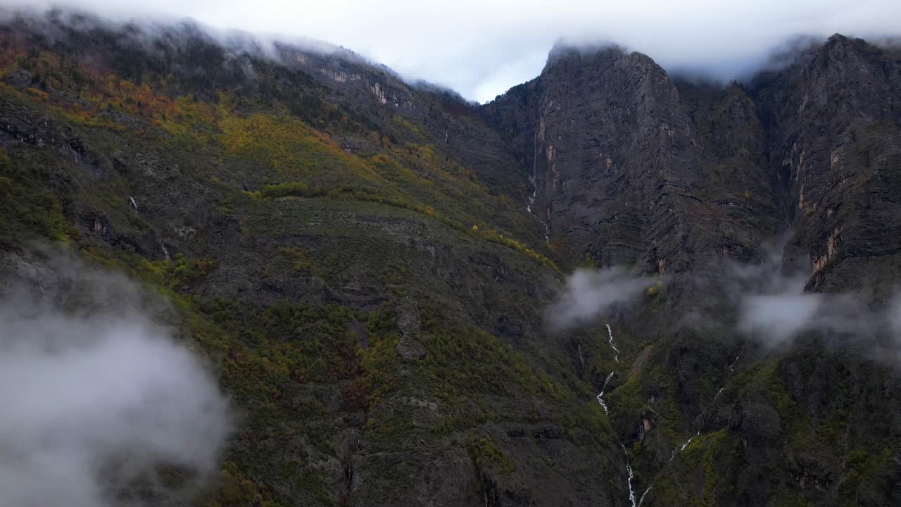 día brumoso en montañas alpinas con nubes que se elevan desde el valle sobre arroyos y follaje colorido