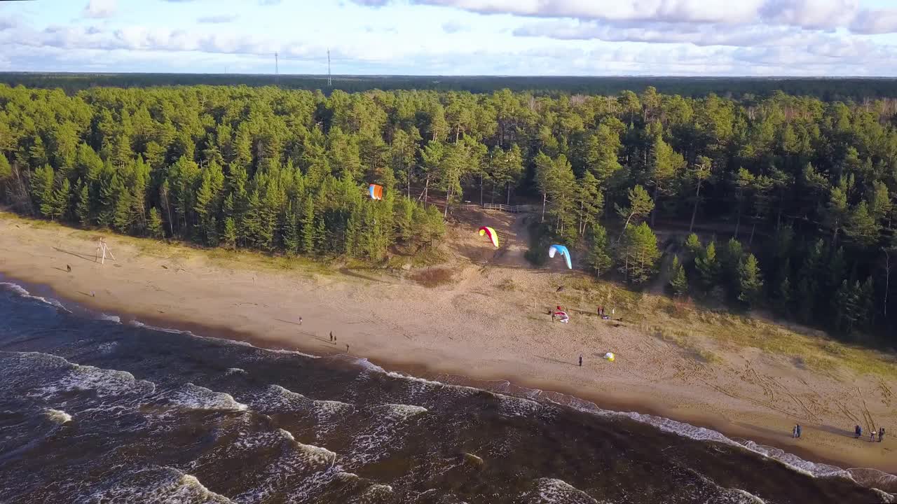 turistas disfrutando del parapente en la playa de arena con olas tranquilas que llegan a la orilla