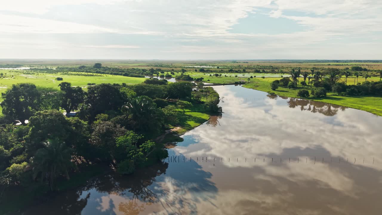 Drone che vola sopra un fiume fangoso che serpeggia attraverso una vasta savana verde con i riflessi del cielo