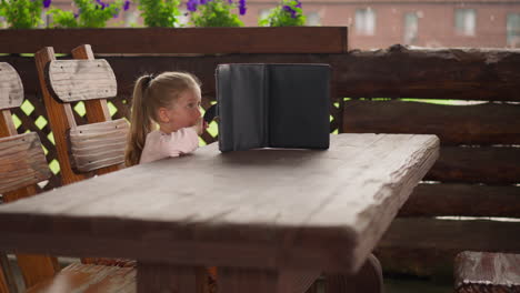 Little-girl-with-tablet-sits-and-waits-rain-end-in-cafe