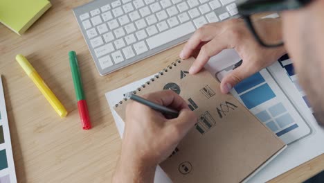 close-up of designer's hand drawing logos in notepad working at desk in office
