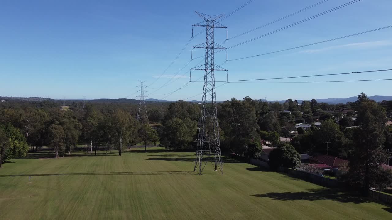 Drone ascending from a green park with trees near high voltage powerlines and near a subdivision with private homes in Australia
