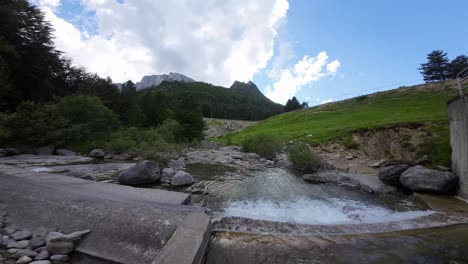 Eine-Drohne-überquert-Im-Flug-Einen-Fluss,-Passiert-Eine-Brücke-Und-Erreicht-Einen-Damm