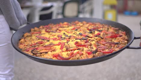 carrying paella to a gathering of people celebrating. spanish traditional dish coocked on a pan with meat, pepper and rice.