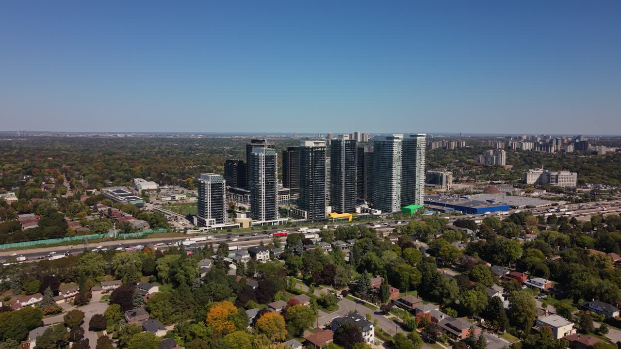 Szerokie ujęcie z powietrza na panoramę wieżowców, otoczoną dzielnicami mieszkalnymi i otwartymi, zielonymi obszarami nad autostradą