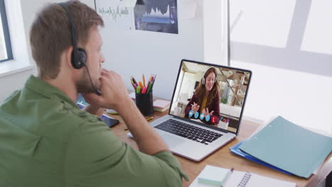 Caucasian-man-wearing-phone-headset-having-a-video-call-with-female-colleague-on-laptop-at-office