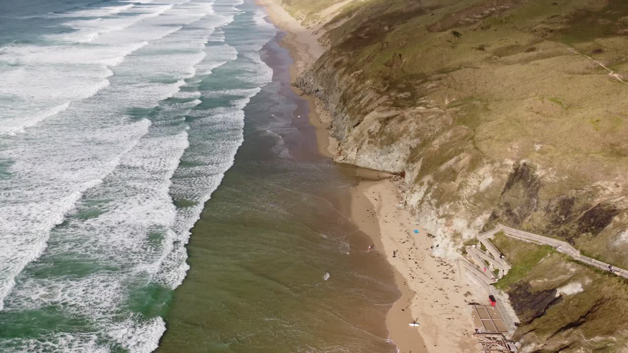 una larga playa de arena dorada con hermosas olas verdes rompiendo en tierra en cornualles