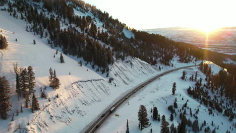 Aerial-View-of-Teton-Pass-Highway-on-Sunny-Winter-Evening,-Wyoming-USA,-Traffic-and-Snow-Capped-Hills