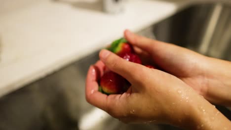 hands washing strawberries under running water