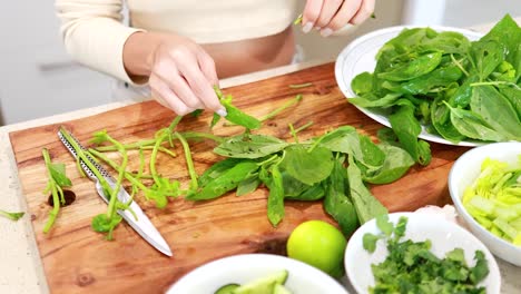 hands skillfully prepare fresh basil on a wooden board in a well-lit kitchen, surrounded by vibrant green ingredients