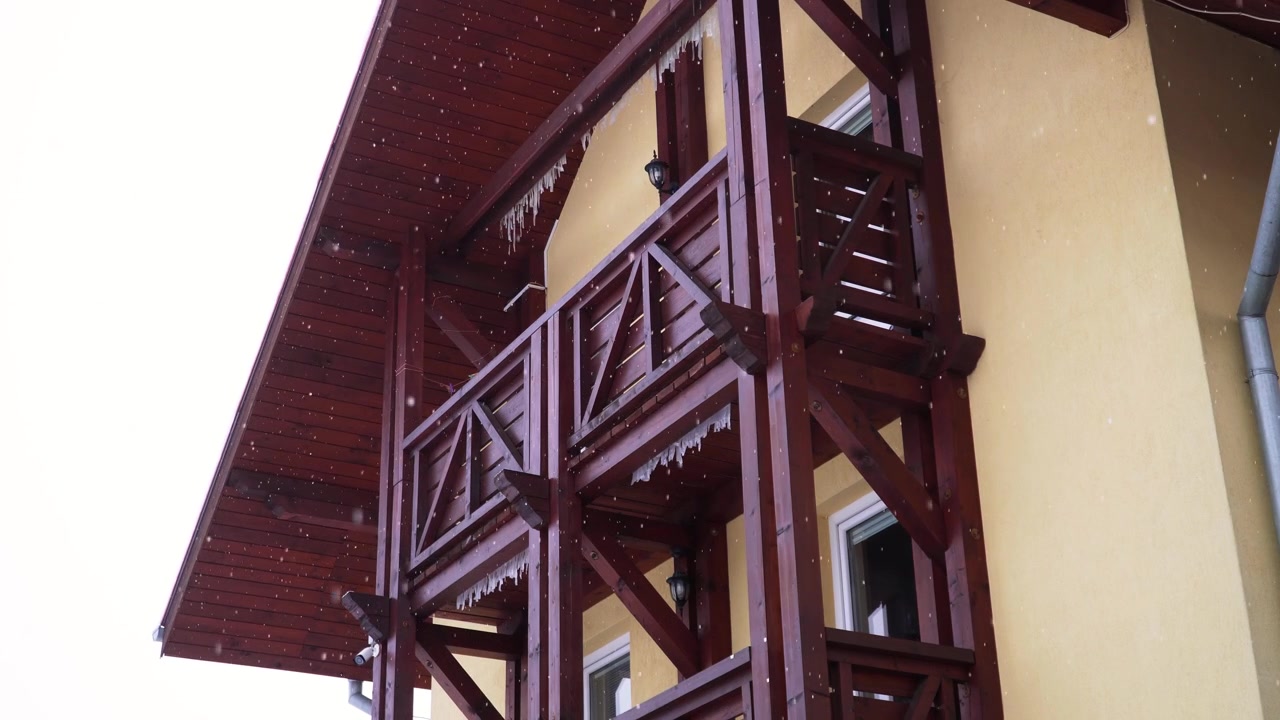 the shot of a brown wooden balcony of a Slovakian house while snowing outside in Slovakia in winter