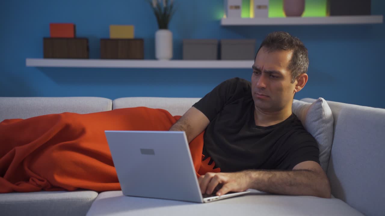 Unhappy man using laptop lying down.