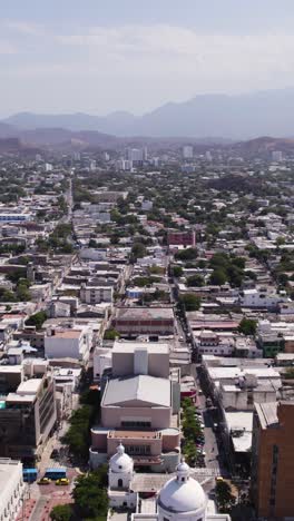 urban landscape of santa marta in colombia, featuring buildings, streets, and trees. aerial, vertical video, dolly right