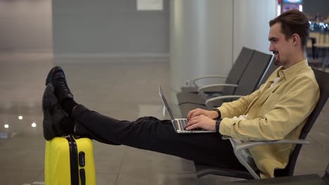 a young bearded man is sitting at the airport, waiting for the plane to depart and using a laptop. having a video conversation