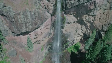 aerial view of a big waterfall in a rocky mountain with a lot of pine trees