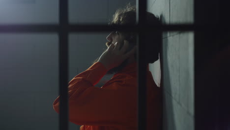 prisionero con uniforme naranja hablando por teléfono en la celda de la prisión